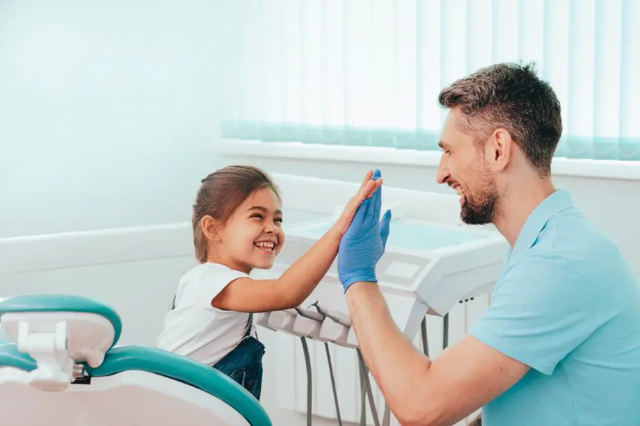 Young girl smiling and giving a high-five to a male dental hygienist in a dental office setting.