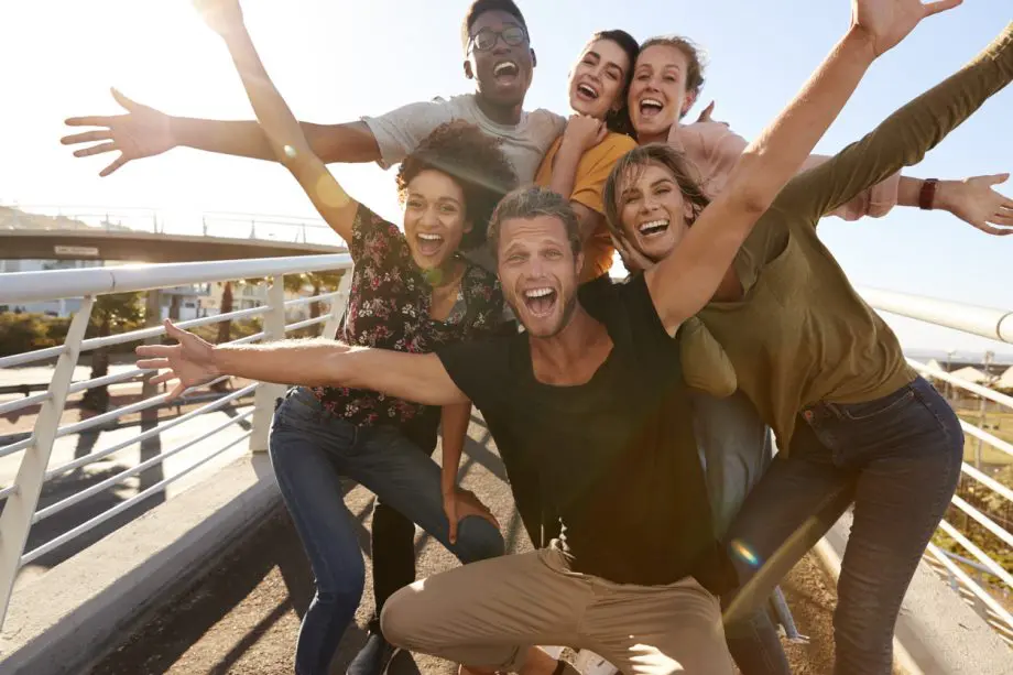 Photograph of a group of friends with their arms thrown open smiling and laughing outdoors.