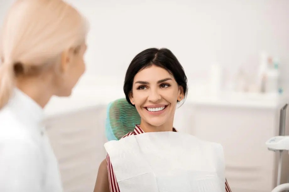 female patient sitting in dental exam chair smiling at female dentist