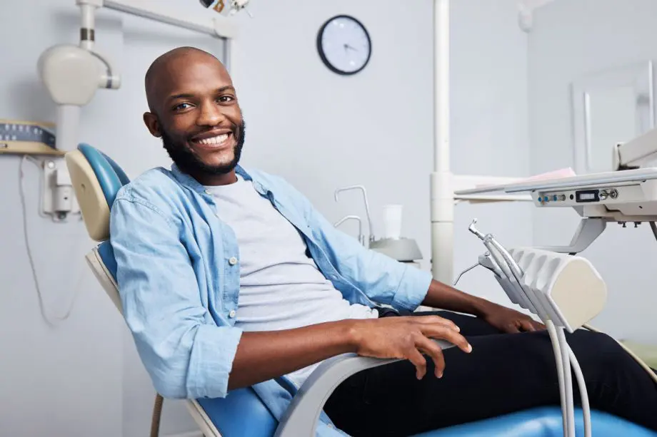 male patient sitting in dental exam chair, relaxed and smiling
