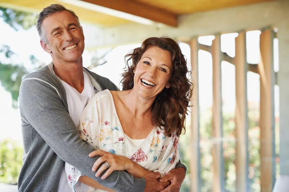 middle-aged couple outside on porch, smiling and hugging each other