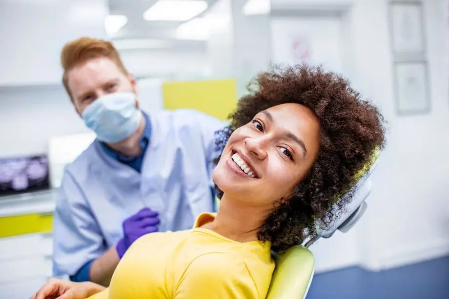 smiling female patient in foreground in dental chair with dentist in background